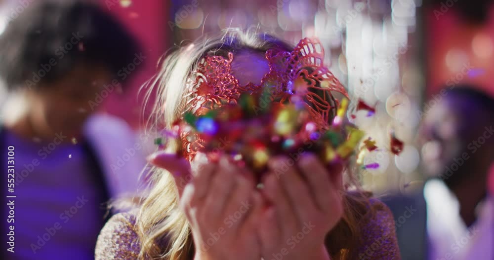 Video of happy caucasian woman in masquerade mask blowing glitter to camera at a nightclub