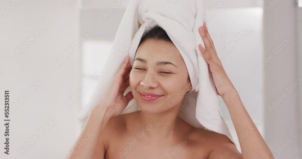 Video of portrait of smiling biracial woman with towel on hair looking in mirror in bathroom Video of portrait of smiling biracial woman with towel on hair looking in mirror in bathroom
