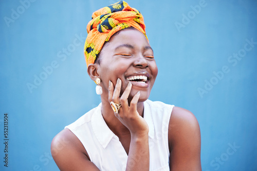 Obraz na plátně Happy black woman, african fashion and culture with turban scarf on blue wall background in Nigeria