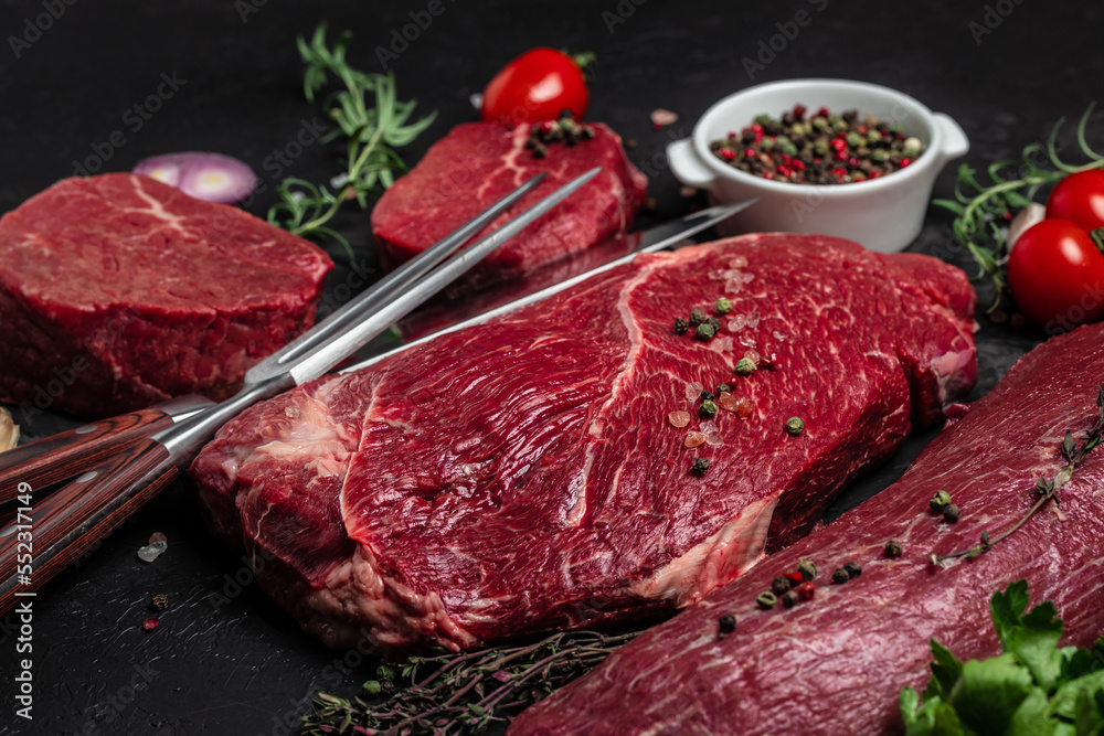 Variety of fresh raw beef steak with spices for grilling on a dark background. Whole piece of steaks ready to cook. banner, menu, recipe place for text, top view