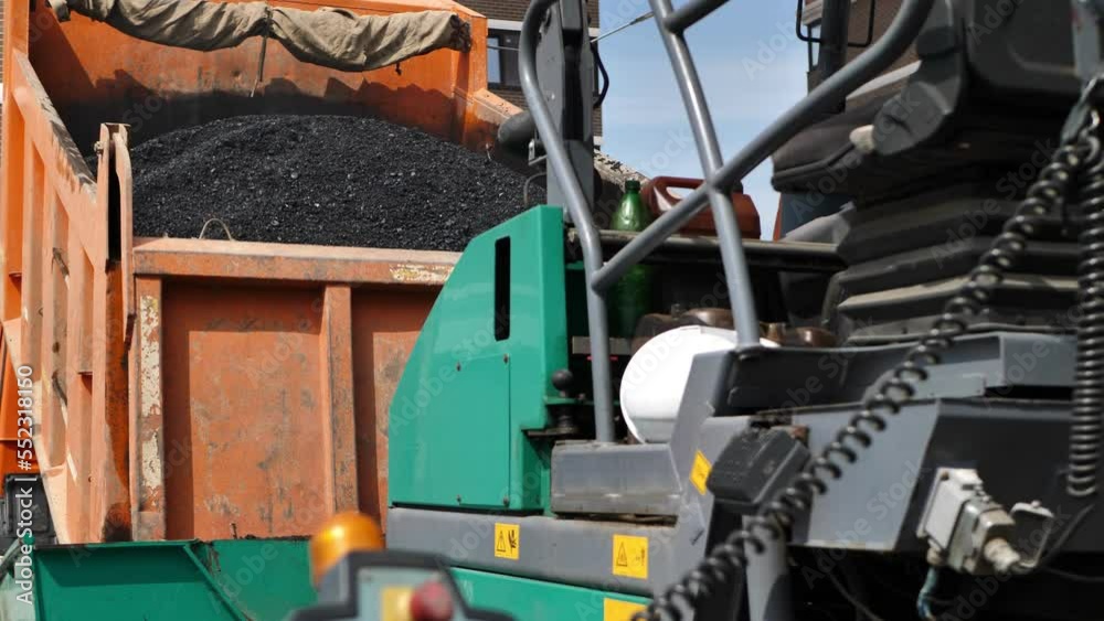 Construction of a new road, a truck pours hot asphalt into the bucket of an asphalt paver. Construction of a new road, a truck pours hot asphalt into the bucket of an asphalt paver.