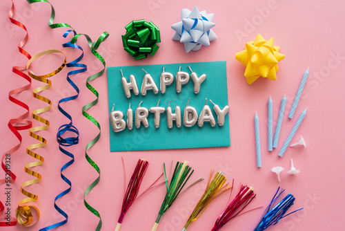 Photography Top view of festive candles in shape of Happy Birthday lettering near serpentine and drinking straws on pink background