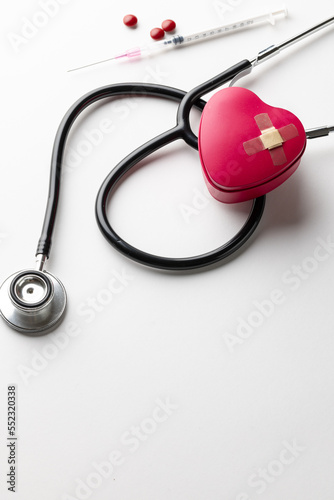 Vertical of stethoscope, heart with sticking plasters, syringe and pills, on white with copy space