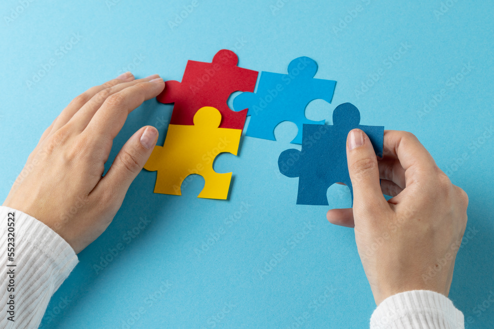 Composition of hands putting jigsaw puzzle pieces together on blue background with copy space Composition of hands putting jigsaw puzzle pieces together on blue background with copy space