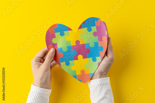 Composition of hands holding jigsaw puzzle heart on yellow background with copy space