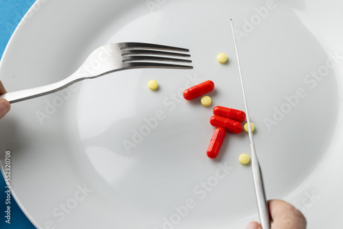 Composition of hands holding fork and knife over plate with various pills