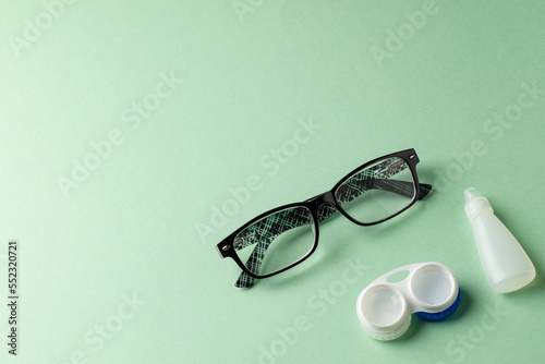 Fototapeta Naklejka Na Ścianę i Meble -  Composition of glasses with eye drops and contact lenses on green background