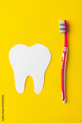 Vertical composition of white tooth and toothbrush on yellow background with copy space