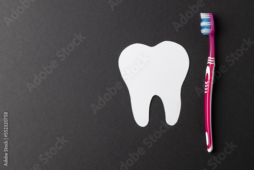 Composition of white tooth and toothbrush on black background with copy space