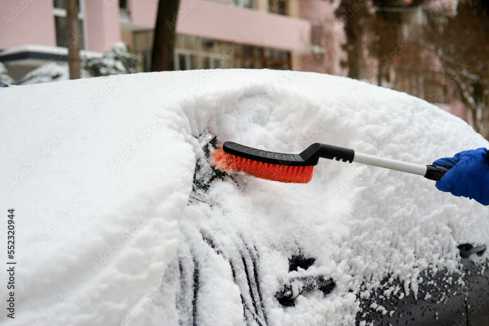 a hand in a blue glove using a special brush cleans a thick layer of snow that covered the car a hand in a blue glove using a special brush cleans a thick layer of snow that covered the car