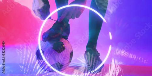 Low section of player tying shoelace on ball with illuminated circle and plants, copy space