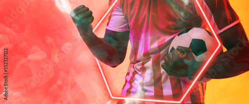 Midsection of african american male player holding ball by illuminated hexagon over smoky background