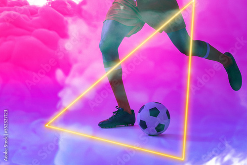 Low section of caucasian male player kicking ball by illuminated triangle over smoky background