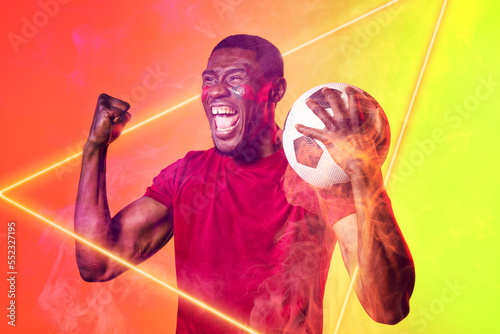 African american cheerful player holding ball screaming by illuminated triangle, copy space
