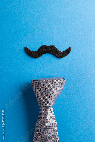 Composition of fake moustache and tie on blue background with copy space