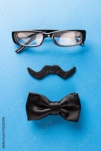 Composition of fake moustache with glasses and bow tie on blue background with copy space