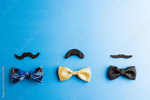 Composition of fake moustaches and bow ties on blue background with copy space