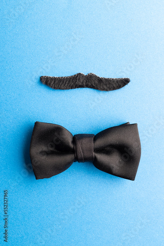 Composition of fake moustache and bow tie on blue background with copy space