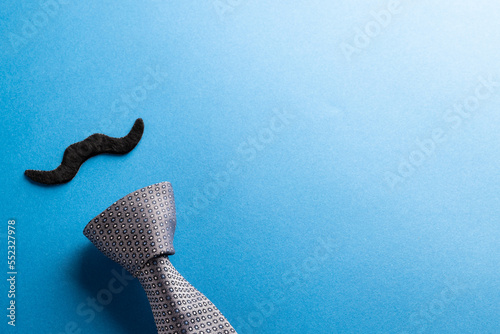 Composition of fake moustache and tie on blue background with copy space