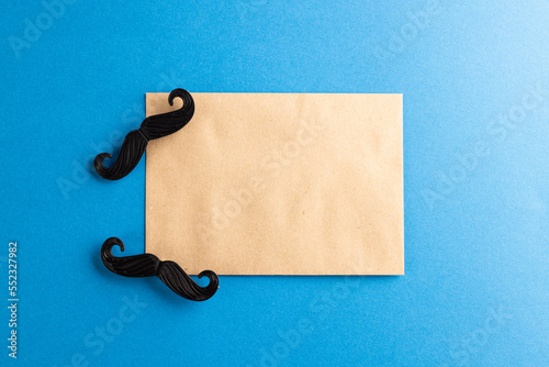 Composition of fake moustaches and envelope on blue background with copy space