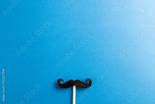 Composition of fake moustache on stick on blue background with copy space