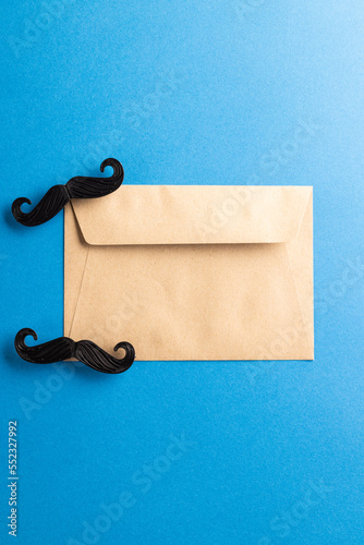 Composition of fake moustaches and envelope on blue background with copy space