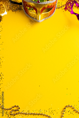 Composition of colourful mardi gras beads and carnival masks on yellow background with copy space
