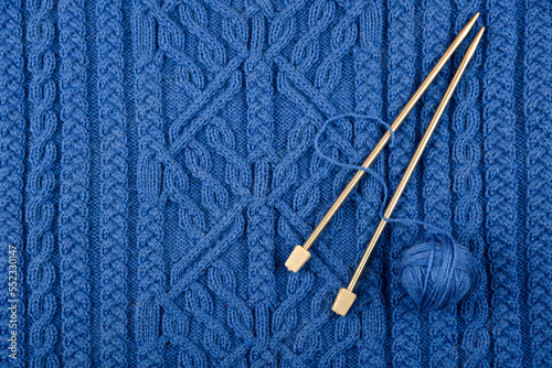 Ball of thread and knitting needles lie on a blue knitted fabric. The concept of spending time at home and knitting warm clothes for winter and autumn.