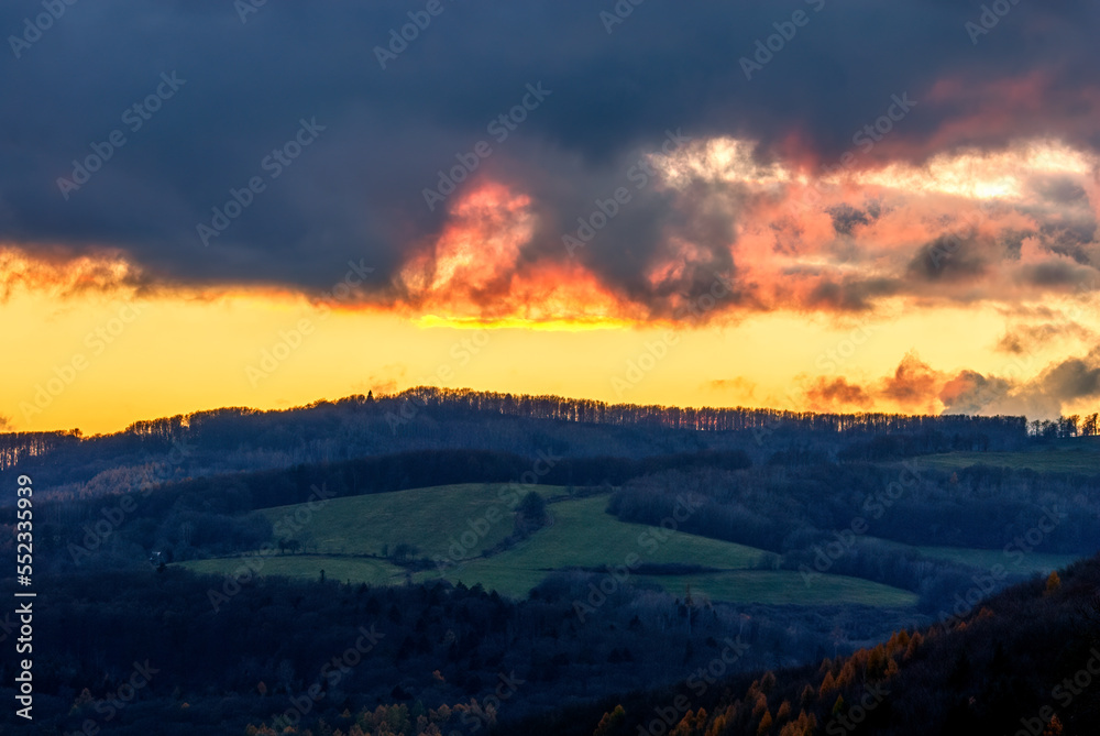 Rural evening landscape with mixed forest after sunset. Beautiful colorful sky with fiery clouds. View of the valley. Late autumn. Dubrava, Slovakia.