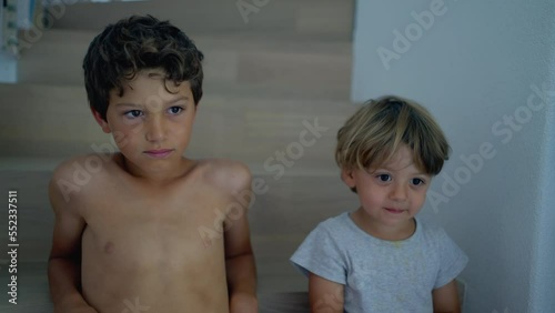 Two young brothers sitting at home staircases. Siblings together. Candid authentic family moment. Older brother hanging out with younger boy