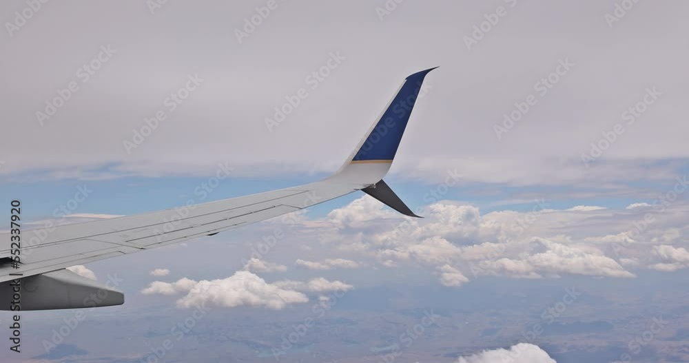 Through window, we observe an airplane wing flying above skies against background of fluffy clouds as viewed horizon Through window, we observe an airplane wing flying above skies against background of fluffy clouds as viewed horizon