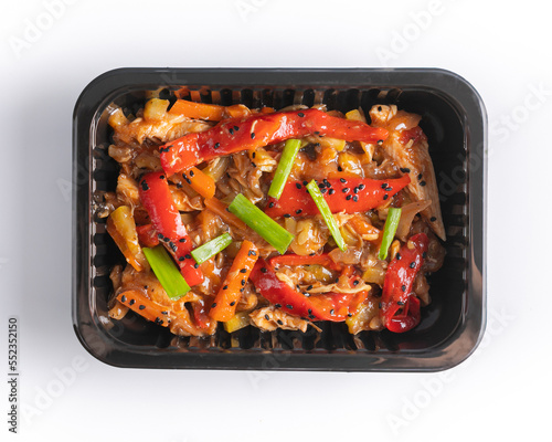 Chineese style chicken in sweet and sour sauce with paprika and carrots in black plastic box for  delivery top view isolated on white