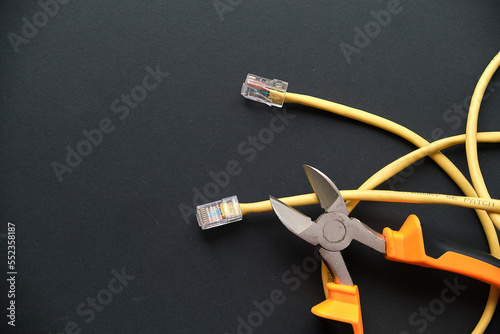 pliers and yellow internet cable on a black background. the concept of turning off wired internet for non-payment.