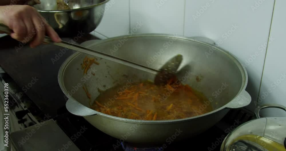 The cook prepares pilaf, takes garlic out of the cauldron on a plate