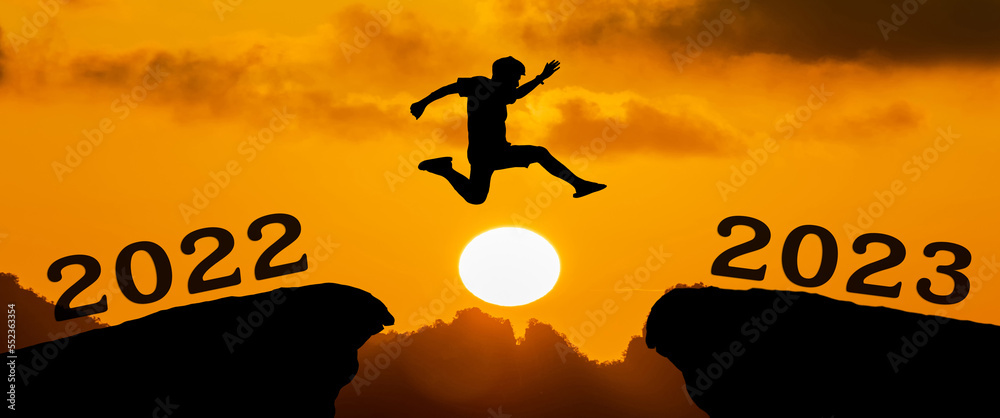 A young man jump between 2022 and 2023 years over the sun and through on the gap of hill silhouette evening colorful sky. happy new year 2023. A young man jump between 2022 and 2023 years over the sun and through on the gap of hill silhouette evening colorful sky. happy new year 2023.