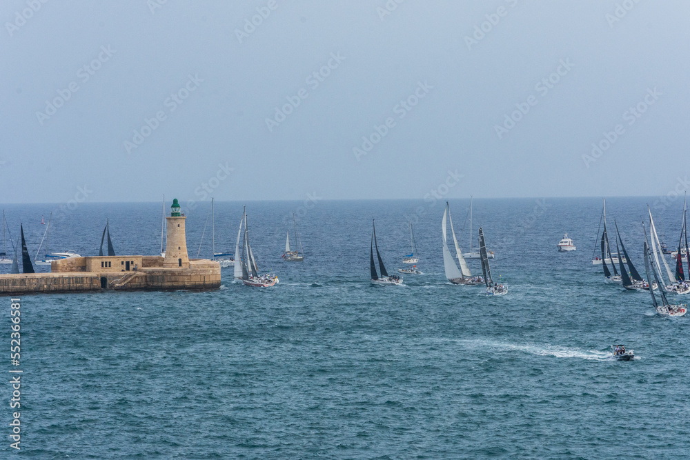 Sailing boats passing the lighthouse on the Valletta Breakwater at the entrance to the Grand Harbour, Valletta, Malta.