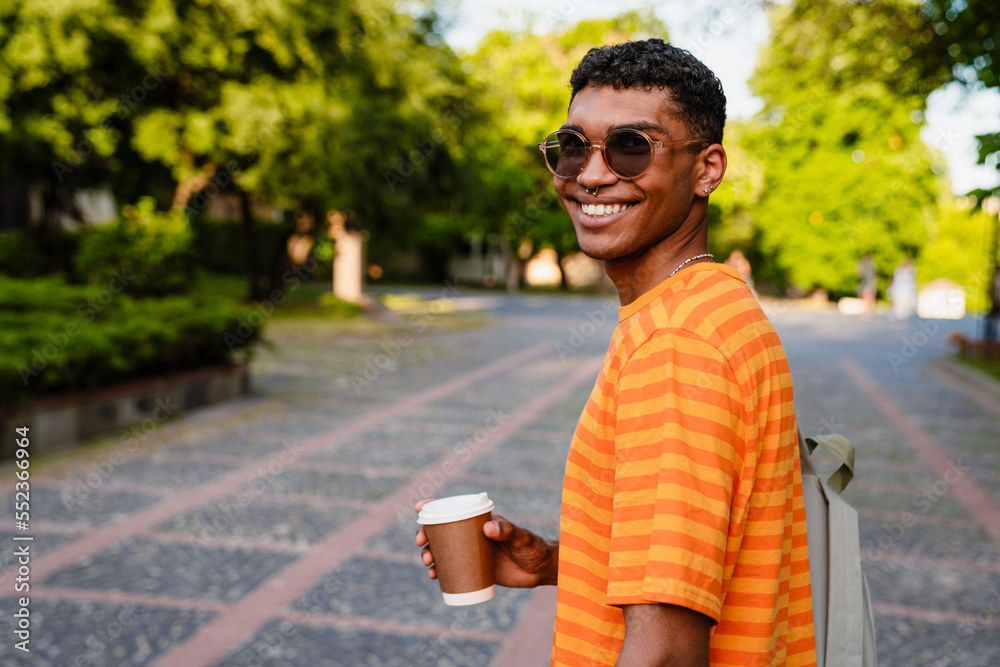 Fototapeta premium Young african man with backpack drinking coffee while standing outdoors