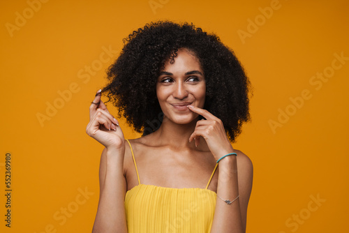 Pensive african american woman wearing dress posing isolated over yellow wall