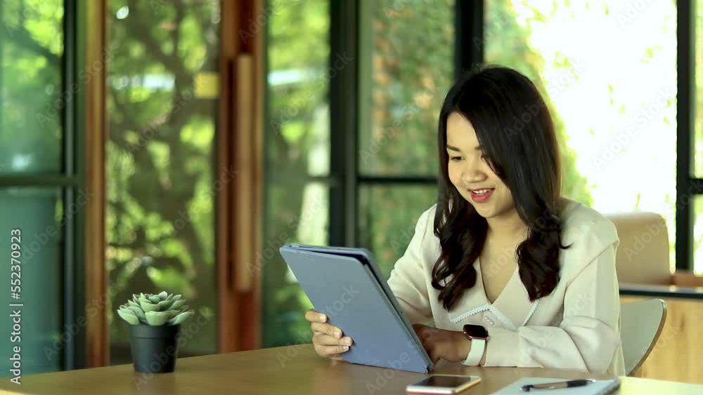 Smiling young Asian businesswoman sitting at the office table using a tablet. she is smiling and happy to work. Smiling young Asian businesswoman sitting at the office table using a tablet. she is smiling and happy to work.