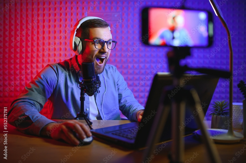 Young man recording or streaming podcast using microphone at his small broadcast studio. Content creator. Young man recording or streaming podcast using microphone at his small broadcast studio. Content creator.