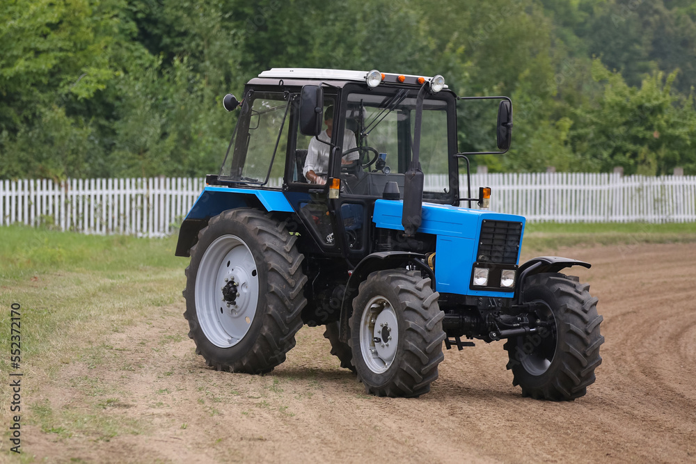 A blue tractor is driving a village road A blue tractor is driving a village road