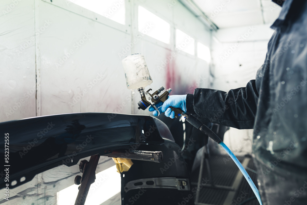 White spray booth interior. Process of automobile painting. Car fender varnishing. Unrecognizable person in protective coveralls using paint spray gun. High quality photo