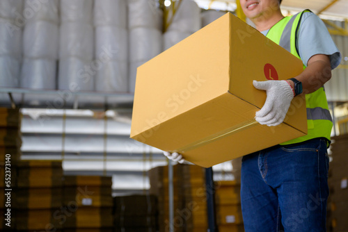 Fotografi Asian male worker lifting cardboard boxes Inside a retail warehouse filled with shelves full of goods and cardboard boxes