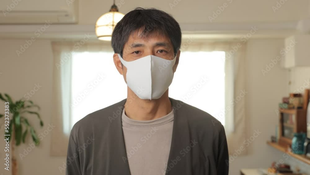 Middle aged asian man with mask on standing still and looks at the camera at home. Reluctant, Tired, Unsatisfied. 25P. Middle aged asian man with mask on standing still and looks at the camera at home. Reluctant, Tired, Unsatisfied. 25P.