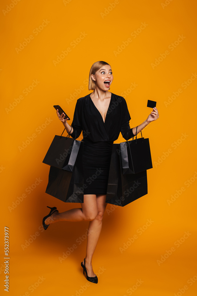 Fototapeta premium Young woman screaming while posing with cellphone and shopping bags