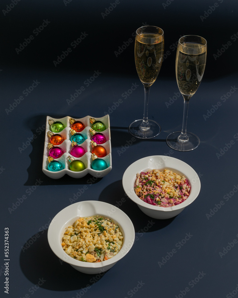 Two traditional russian and ukranian salads: Olivier and herring under a fur coat with champagne and new year decoration  on dark blue background 