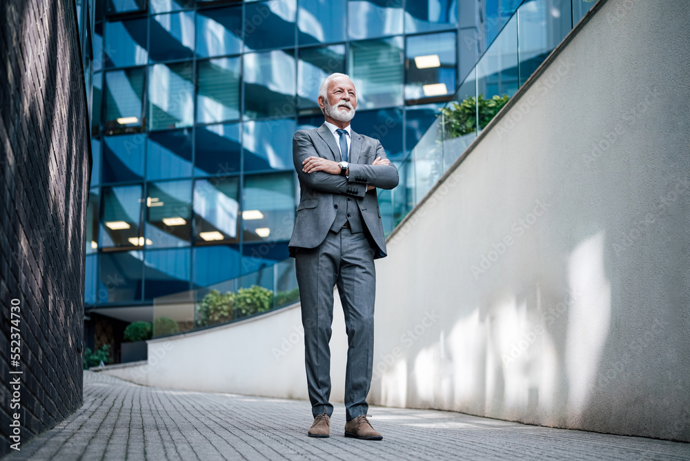 Obraz premium Full length of entrepreneur standing with arms crossed on walkway against business office building.