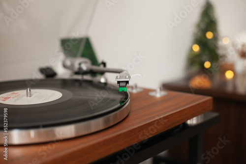 turntable with record playing music on Christmas Day holiday season with yellow bokeh lights. Cozy vintage background.