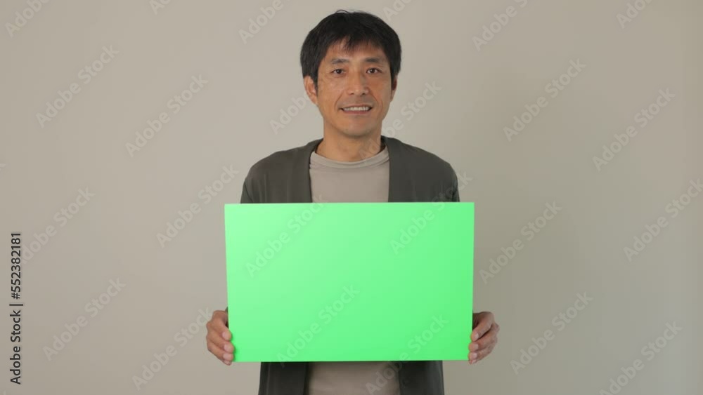 Middle aged asian man holding green board and smiles. For chromakey editing.	