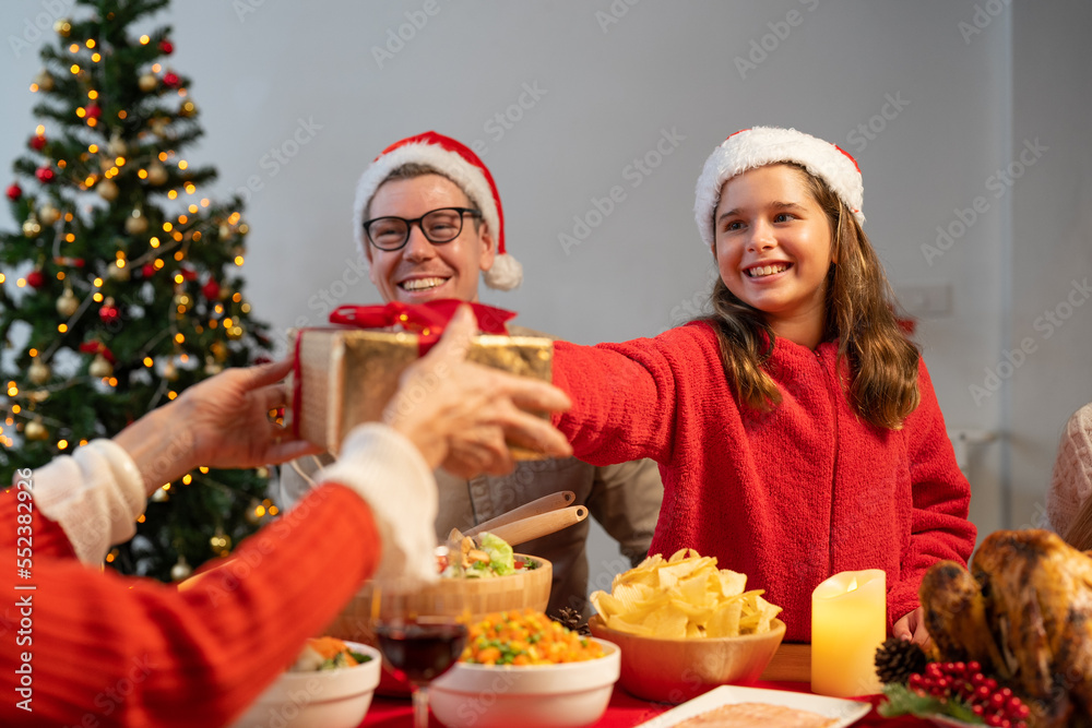 Happy family celebrating Christmas dinner at home. Granddaughter with gift box given to grandmother. Merry Christmas or New Year's eve concept Happy family celebrating Christmas dinner at home. Granddaughter with gift box given to grandmother. Merry Christmas or New Year's eve concept